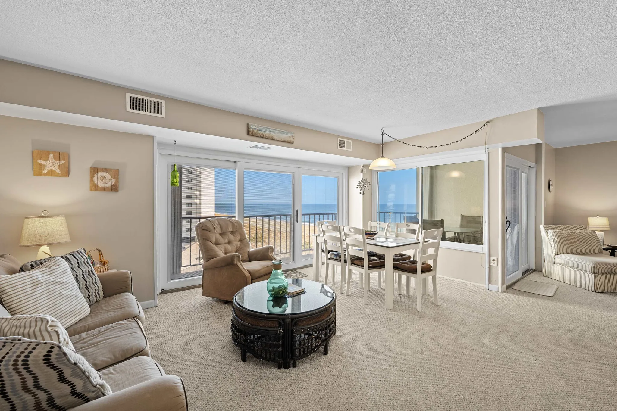 Bright beachfront condo living room with sofa, armchair, dining table and sliding doors opening to an ocean view balcony
