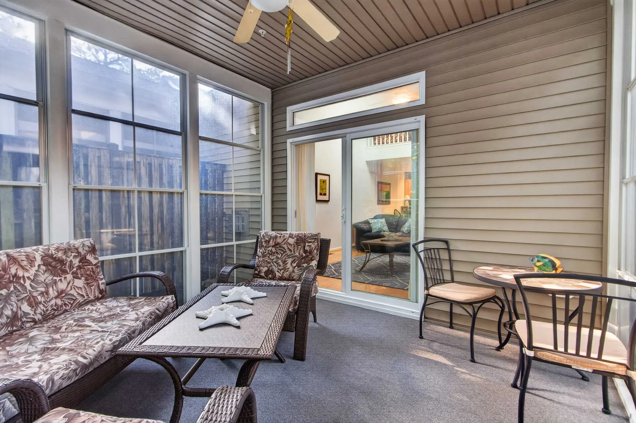 Screened porch with wicker sofa and chairs, ceiling fan, bistro table, and sliding glass doors leading to a living room