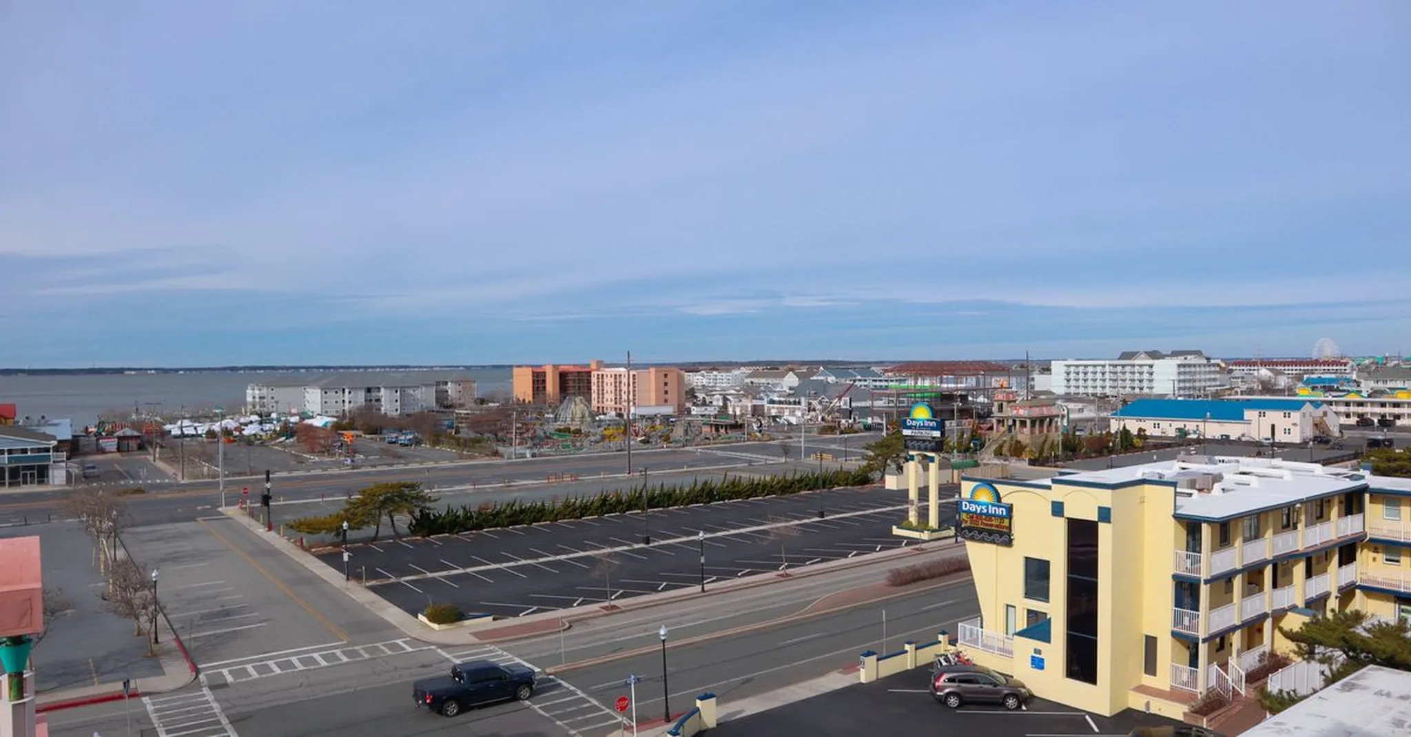 Elevated view of a coastal town with a Days Inn hotel, empty parking lots, low-rise buildings and a bay stretching to the horizon