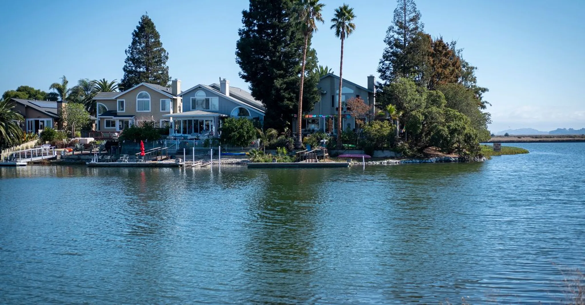 Waterfront homes with private docks and palm trees along a calm blue bay under a clear sky