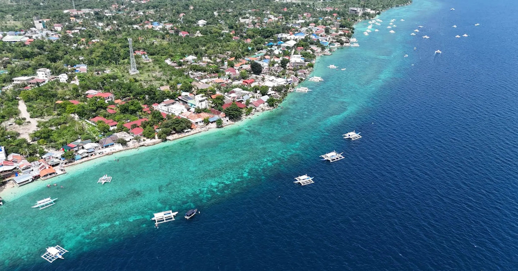 A stunning aerial view of a coastal village, showcasing clear waters and local boats in the Philippines.