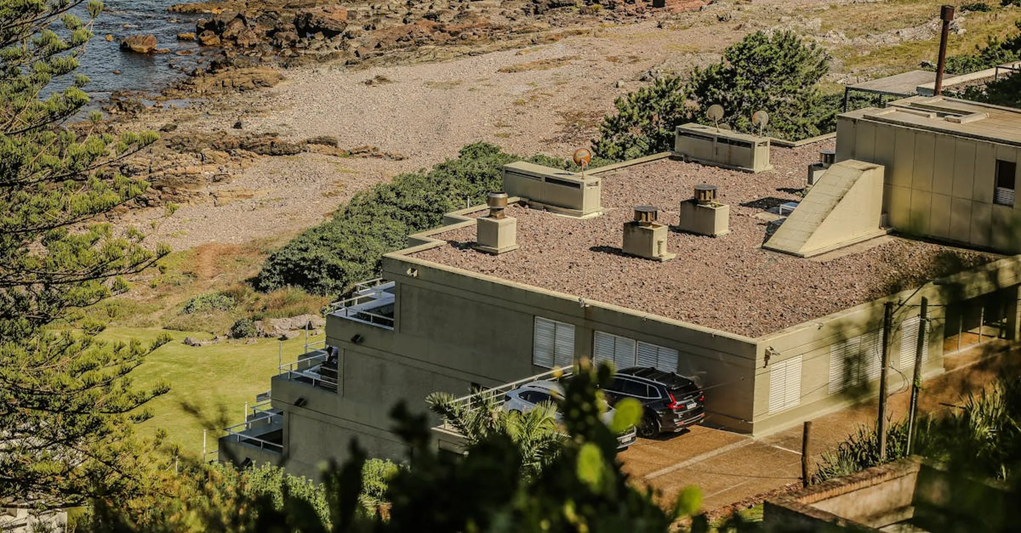 An aerial view of a coastal building with a rocky shoreline in the background.