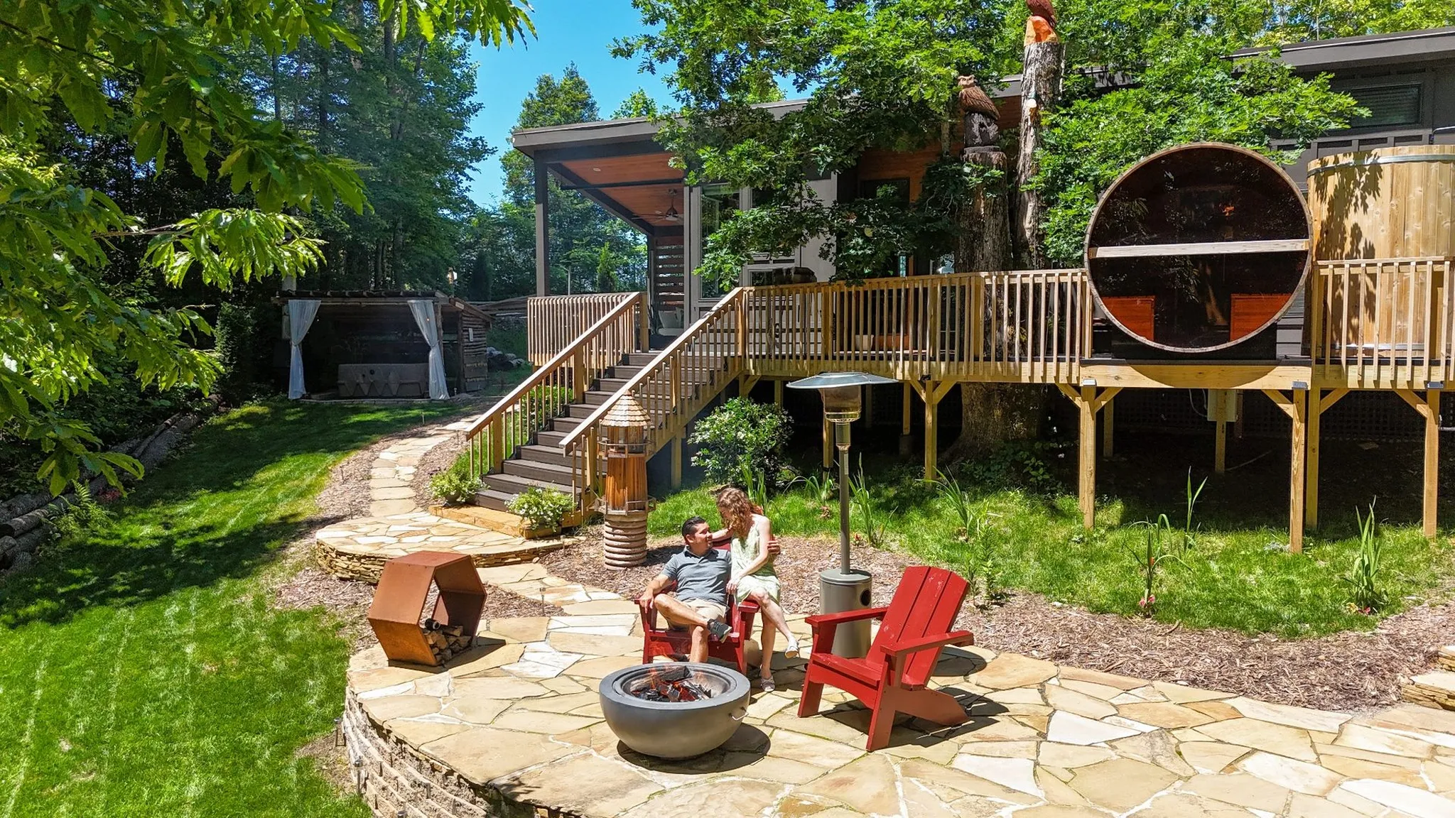 A couple sitting on a flags stone patio in front of a treehouse
