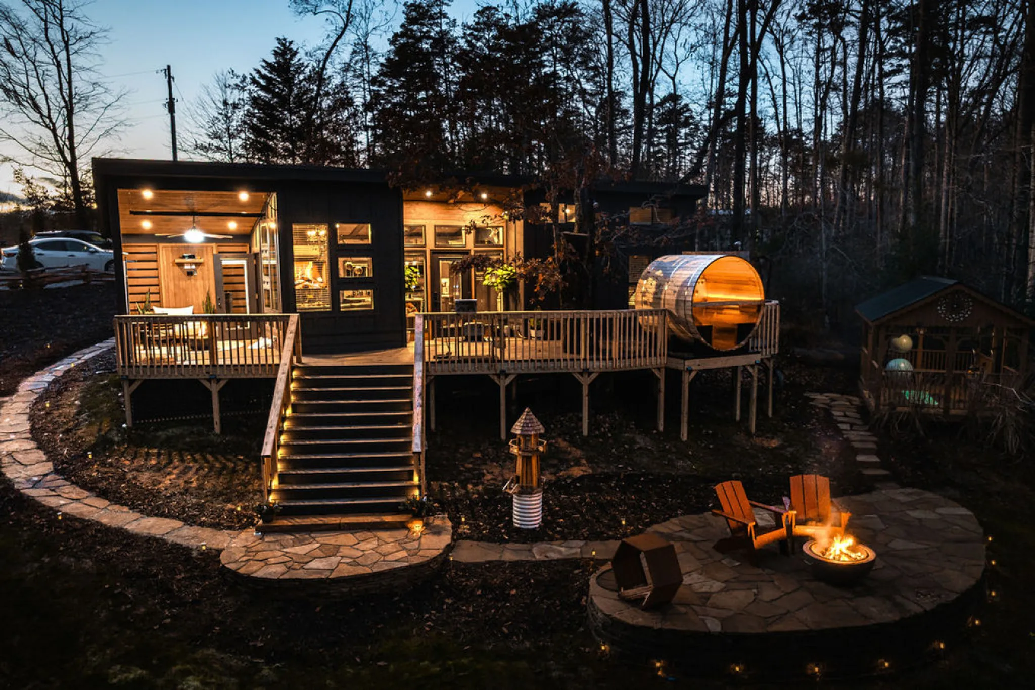 Night shot of a modern cabin with a panoramic barrel sauna and fire pit.