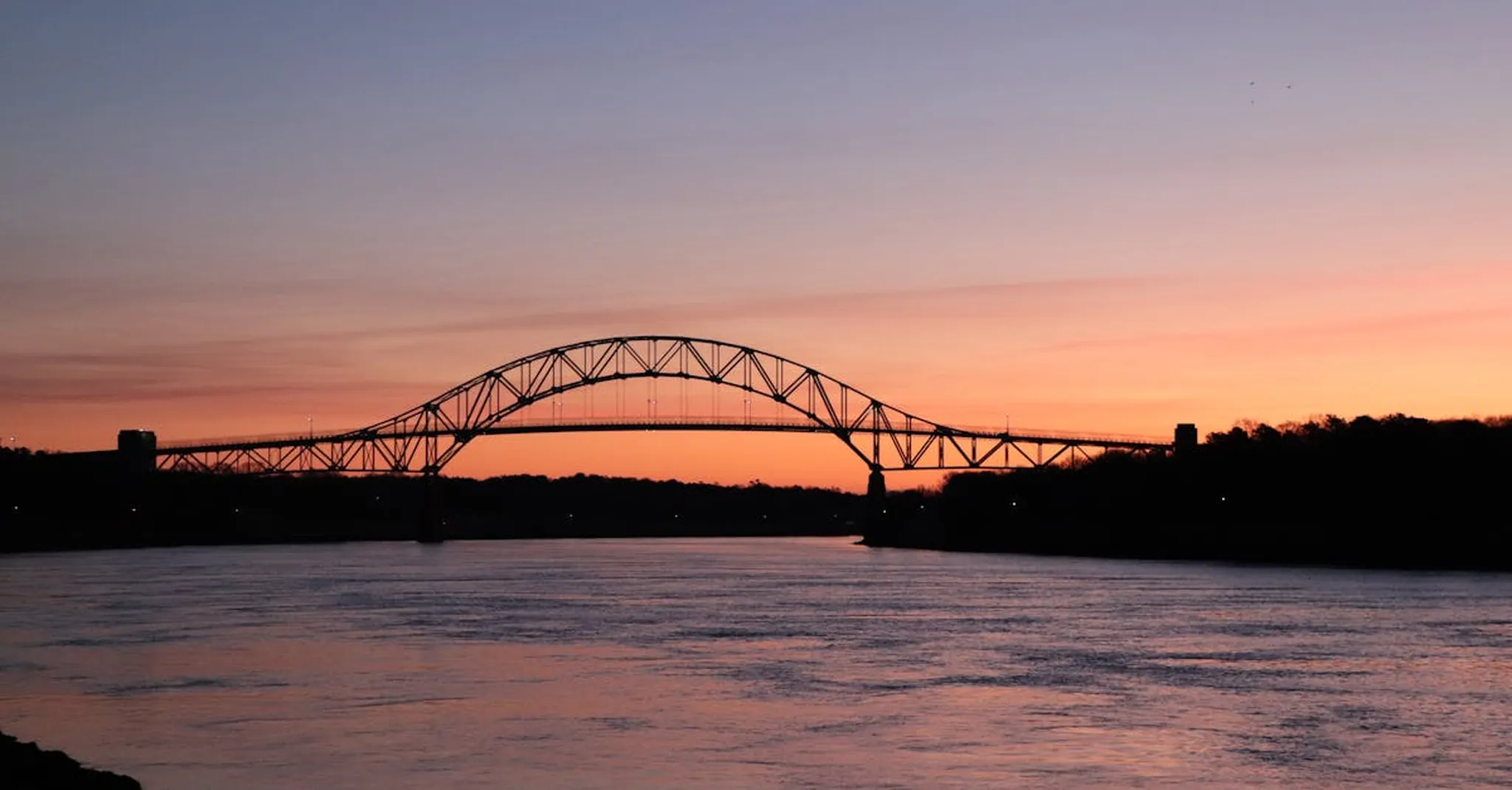 Stunning sunset view of Bourne Bridge silhouetted against the sky over Cape Cod Canal.