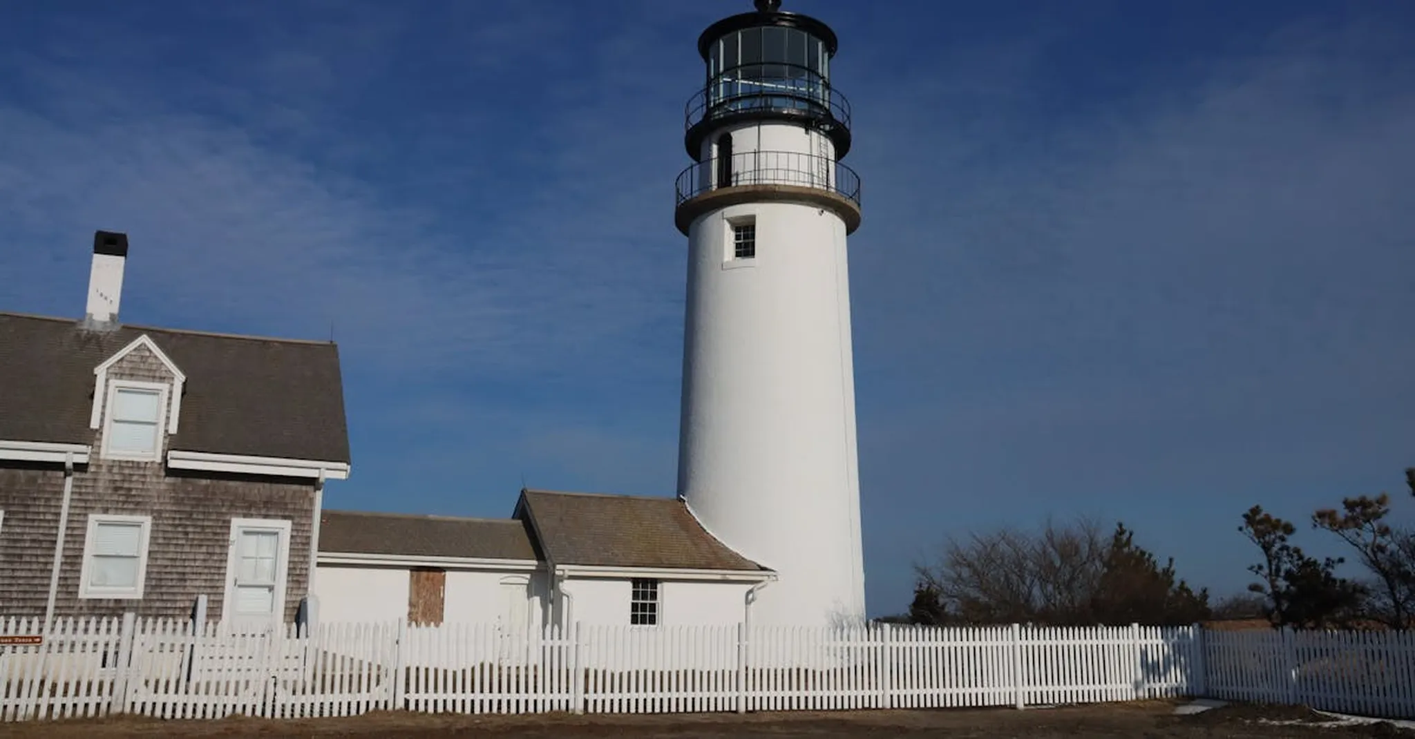 Classic Cape Cod lighthouse at sunrise in Truro, MA, with white picket fence and clear sky.