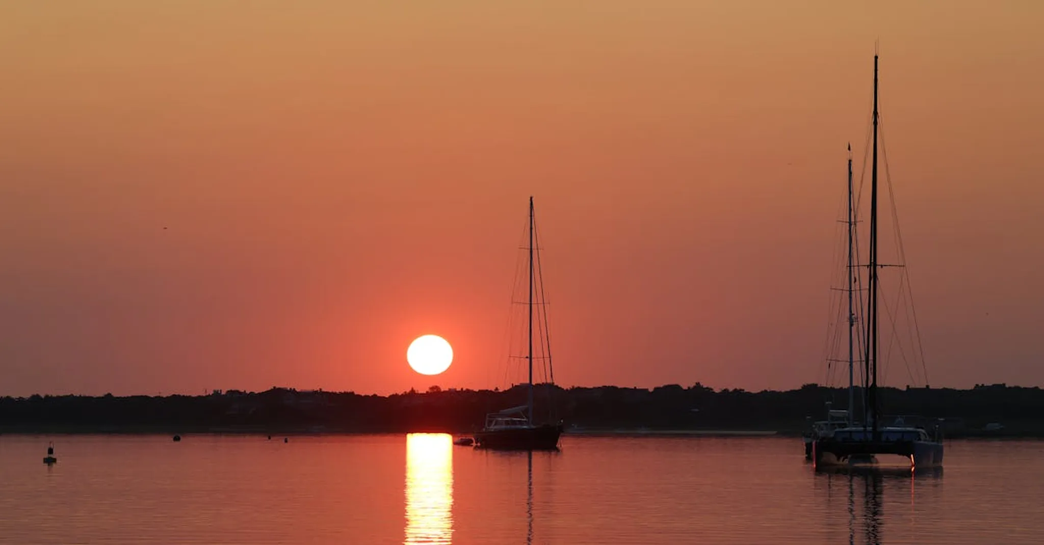 Beautiful sunrise at Brant Point Lighthouse, Nantucket with sailboats on the calm water.