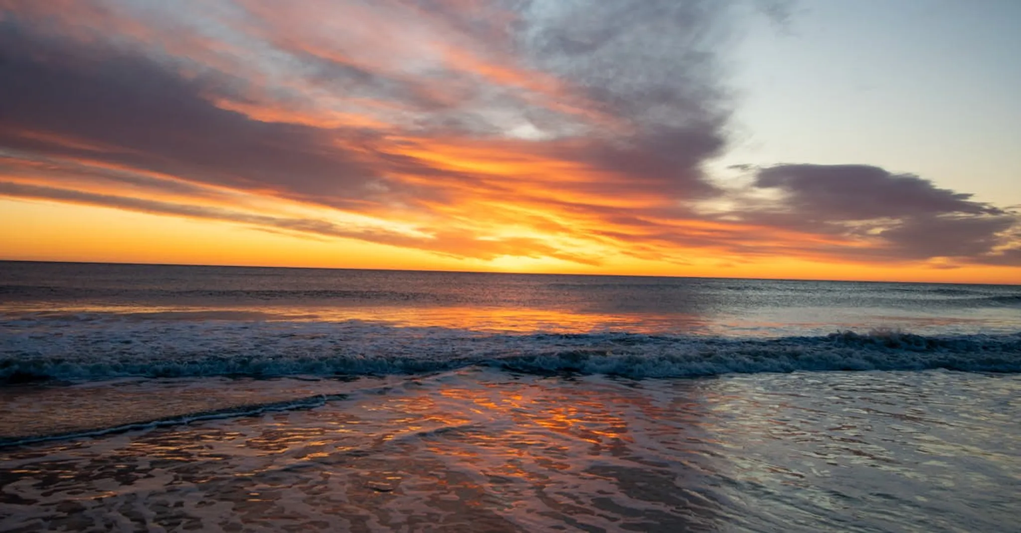 Captivating sunset over the ocean at a Cape Cod beach with vibrant colors reflecting on the waves.