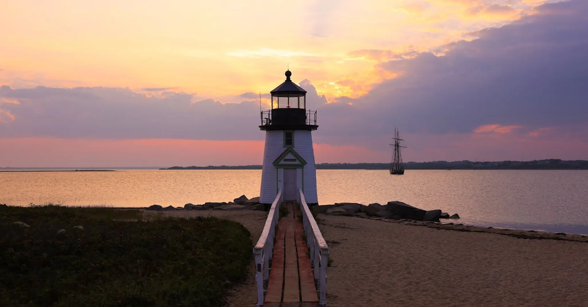 Silhouetted lighthouse at sunset with a tranquil sea in the background.