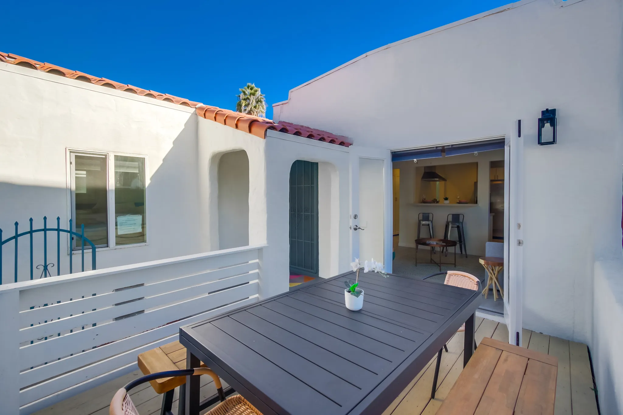 White stucco bungalow entrance with a teal blue door, red tiled step, and tropical plants along a narrow walkway